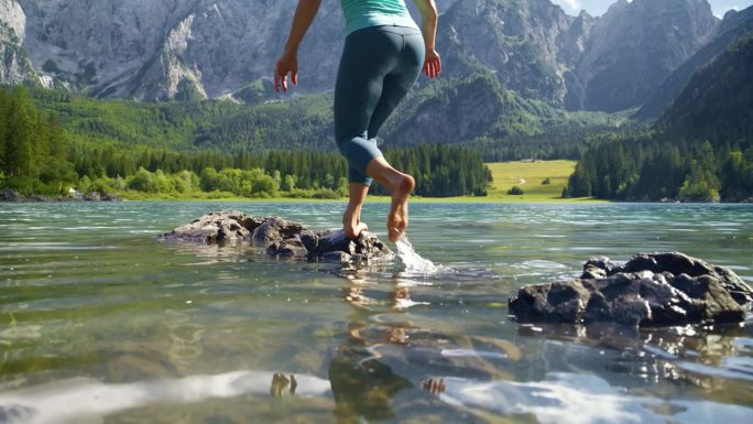 赤脚女子在田园诗般的山间湖泊上踏过岩石