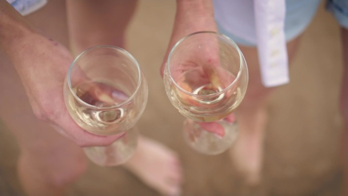 在女人腿和海浪沙滩的散焦背景下，挥舞着玻璃杯中的白葡萄酒