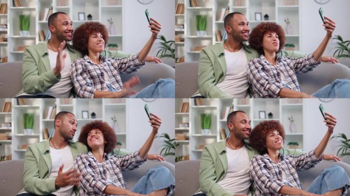 在现代智能手机上进行视频通话时，快乐的非裔美国夫妇互相倚靠。一对热恋的情侣躺在灰色的沙发上，在网上和