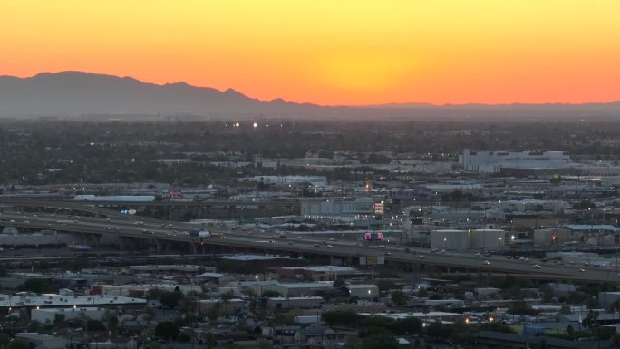 日落时亚利桑那州凤凰城的城市扩张。金色的阳光照耀着群山。零售店和高速公路绵延数英里。