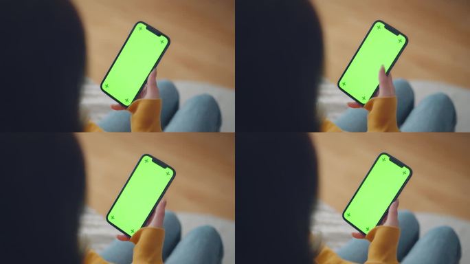 女人手拿着手机，坐在家里的沙发上，拿着智能手机的色度键模型，用空白的绿色屏幕滑动照片或图片