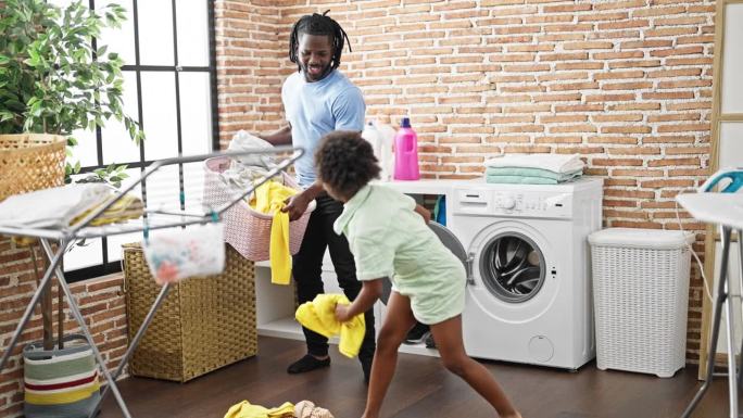 非裔美国父亲和女儿在洗衣房把衣服放在篮子里