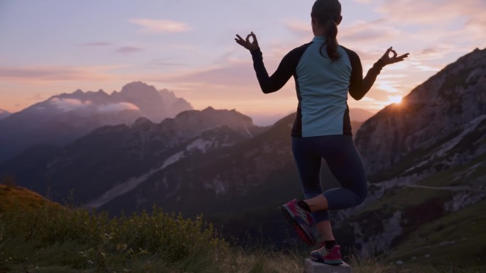 日出时，女子在风景秀丽的山上的岩石上练习瑜伽平衡