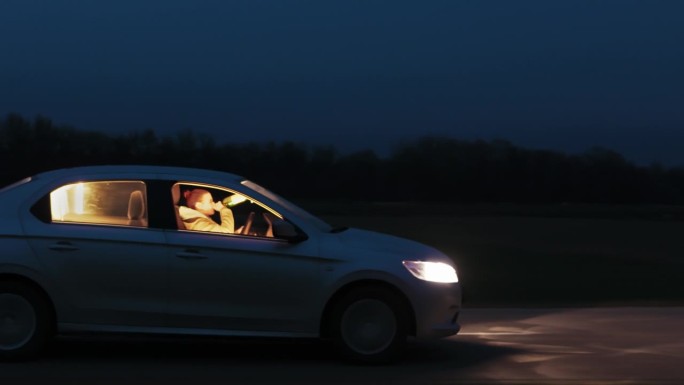 夜间在天空下的路上喝酒开车的年轻女子侧视图