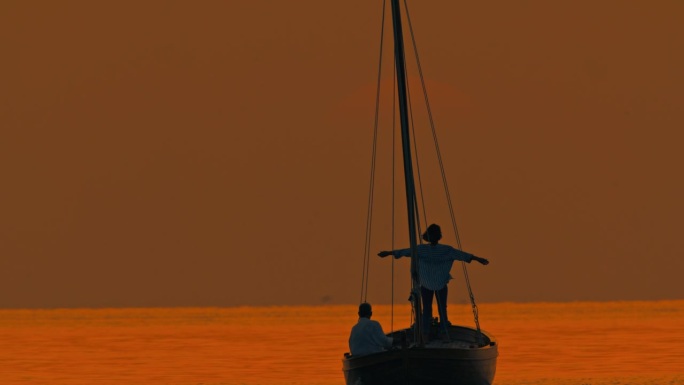 海岸奥德赛:日落时分，一名女子站在船头，伸出双臂，在船上滑行