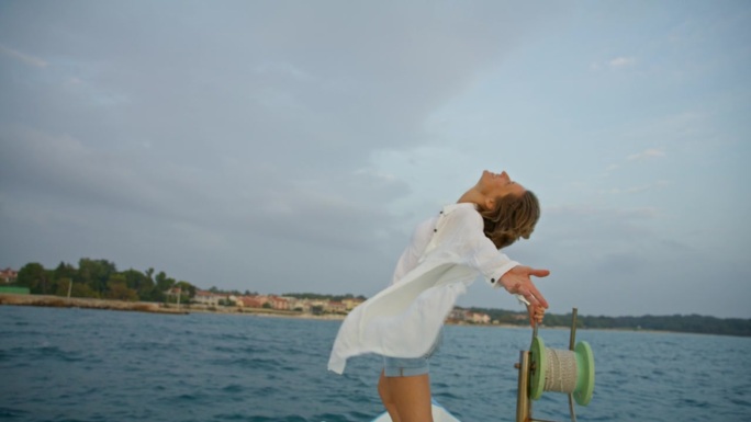 在克罗地亚的一艘帆船上，一名兴高采烈的女游客向后弯腰，伸开双臂站立