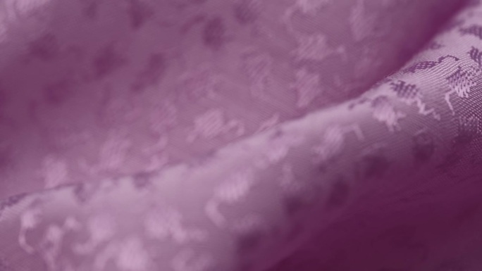 在特写中，淡紫色平纹提花织物的折叠旋转缓慢。材质的宏观纹理。