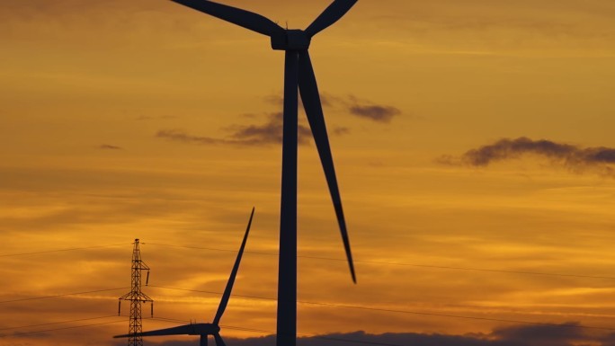 在令人惊叹的多云多彩的日落中，风力涡轮机以风力旋转，以绿色生态的方式产生可再生能源