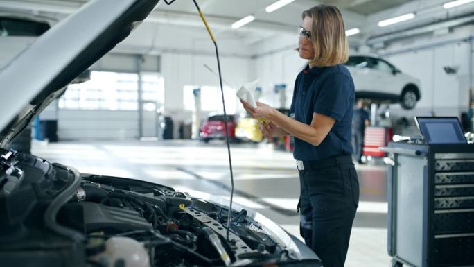 女机械师在汽车修理店检查汽车发动机机油