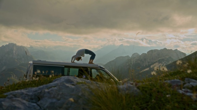 在阳光明媚的偏远山区，一名妇女在货车顶上练习瑜伽
