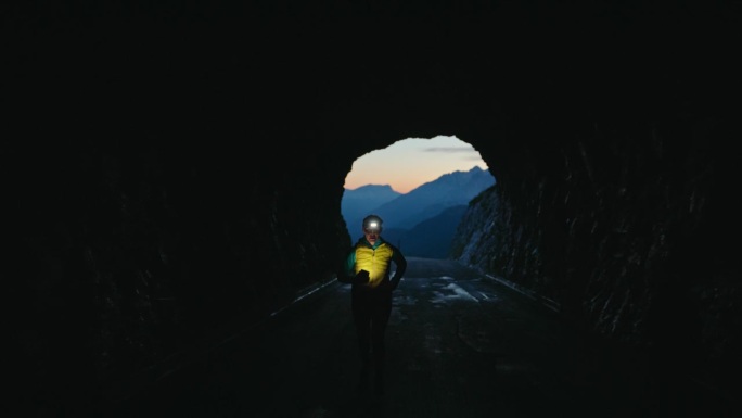 黎明时分，女人打着头灯在黑暗的山间隧道里慢跑。黑暗的场景，戏剧性的场景。
