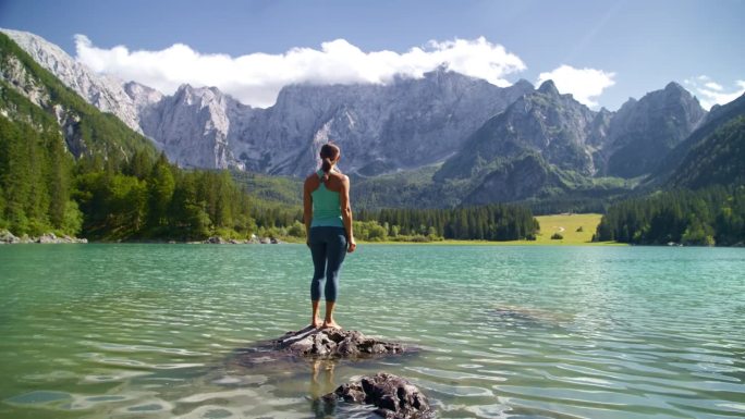 赤脚女子站在湖上的岩石上，欣赏田园诗般的山景。一个女人欣赏美丽的山景。