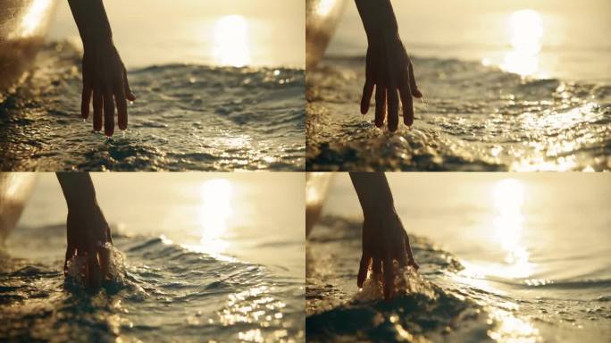 日落时女性的手在船上接触海水的特写