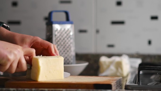 双手在砧板上切马苏里拉奶酪，靠近食物刮刀和白色盘子，水平视频
