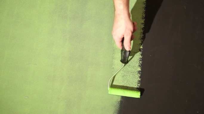 男子用滚筒刷在黑色墙壁上涂绿色颜料，特写。家居装修DIY。手用滚筒刷墙。副本的空间。水性漆。修复。装