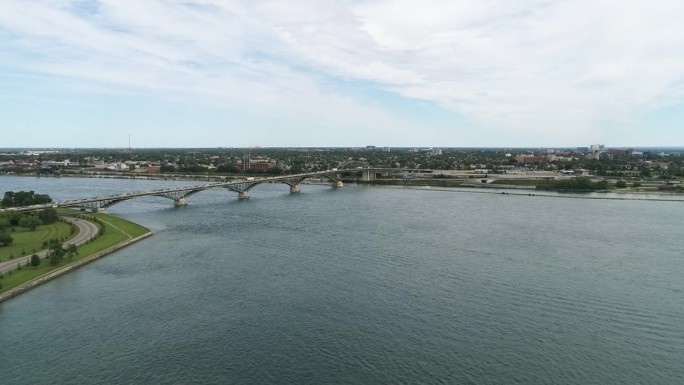 在一个多云的夏日，一架无人机捕捉到了伊利堡和平桥，连接着伊利堡和布法罗，飞过蓝色的水域，背景是城市。