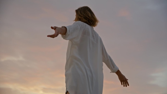 SLO MO海滨日落:女子站在码头上，张开双臂，拥抱美丽的夜空