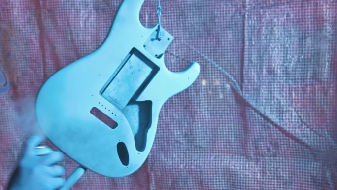 男子用蓝色喷雾罐喷涂电吉他本体。4k视频片段UHD 3840x2160