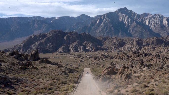白色越野车行驶在一条土路上，驶向沙漠中的东塞拉山脉