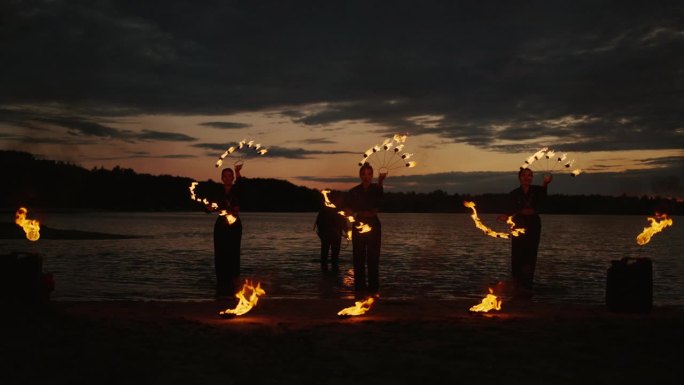 手持火把的特技演员在日落后的海滩上表演火焰表演，令人惊叹的慢镜头