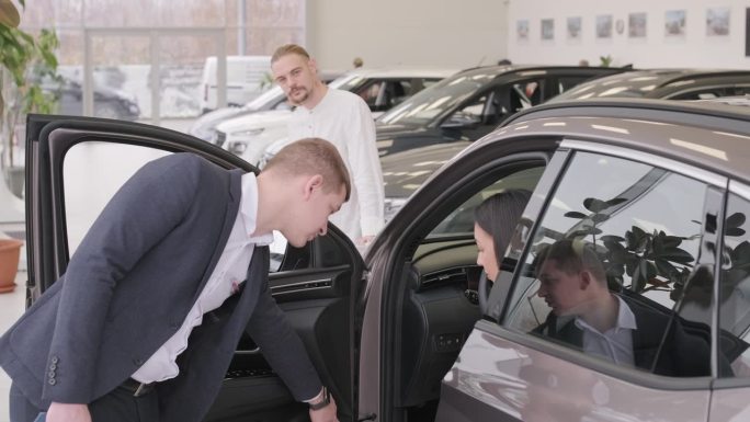 在经销商沙龙上，年轻的汽车推销员向年轻夫妇展示新车。