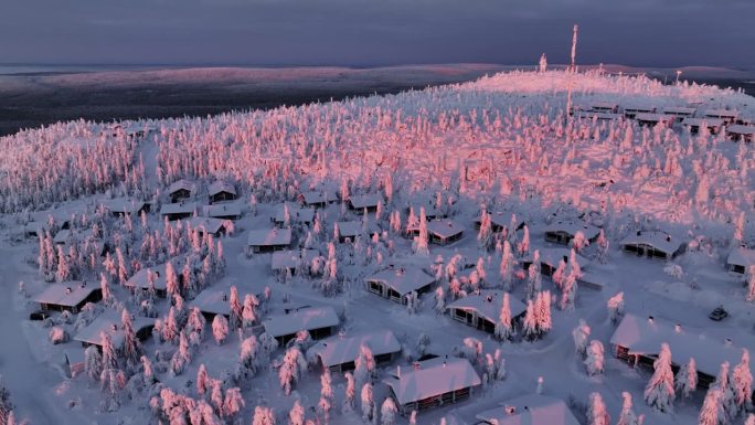 芬兰日出时，无人机在Iso-Syote fjell山顶的雪屋上空盘旋