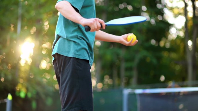 一名男子在户外球场打匹克球，用球拍投球。慢动作