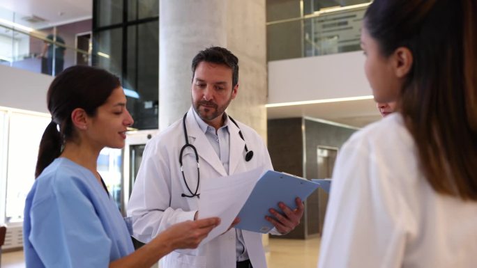 在医院与团队的简短会议中，男医生将表格递给一名医学实习生