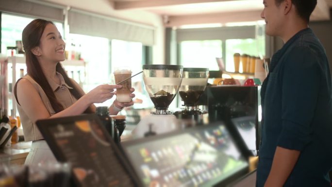 年轻的亚洲服务意识的咖啡师与顾客在咖啡店
