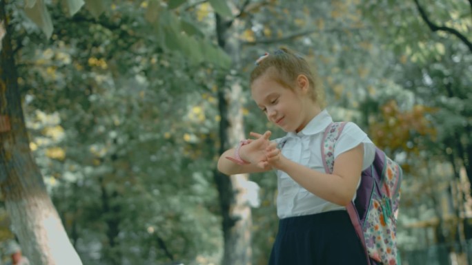 美丽的白人女学生下课后在学校公园户外使用智能手表。快乐的孩子在智能手机上与父母视频通话。带GPS追踪