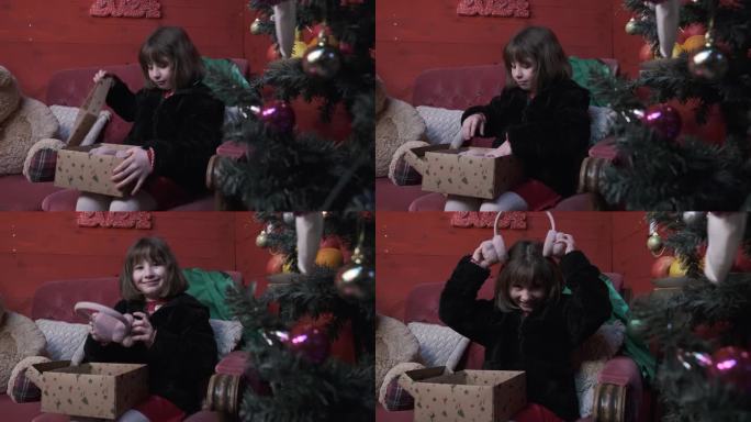 坐在红色扶手椅上的小女孩高兴地打开她的圣诞礼物，满心欢喜