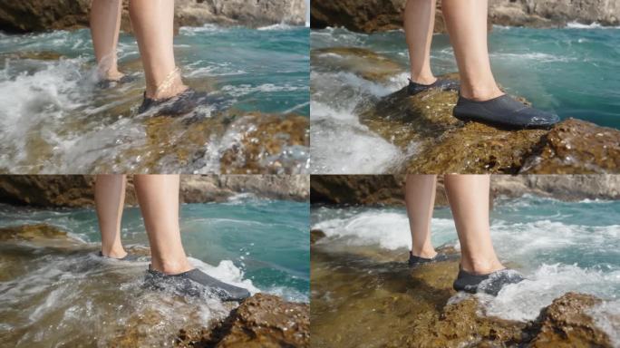 女性脚的特写镜头，她穿着专门为陡峭岩石设计的水鞋，站在岩石悬崖上，波浪覆盖着她的脚。缓慢的运动。