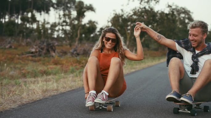 一对夫妇坐在乡村公路上玩滑板，玩得很开心