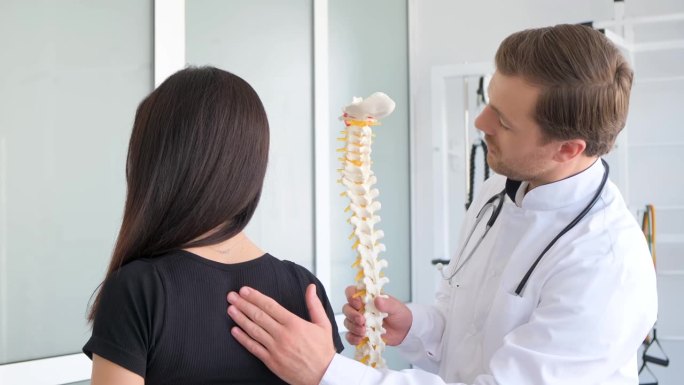 一位年轻女子正在接受脊椎病学专家的检查。一位专业医生检查病人的背部