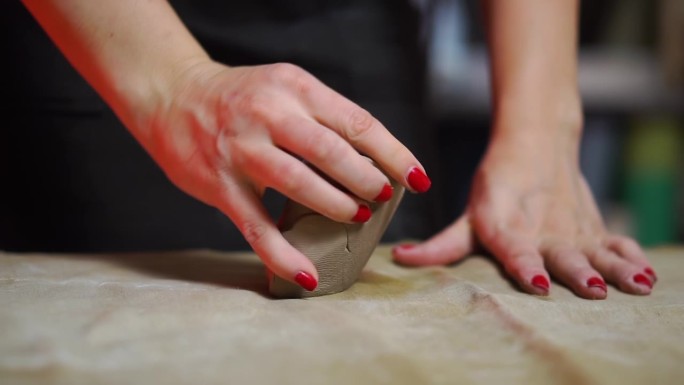 女性的手在桌子上用布料揉捏一块灰色的粘土，制作工艺品