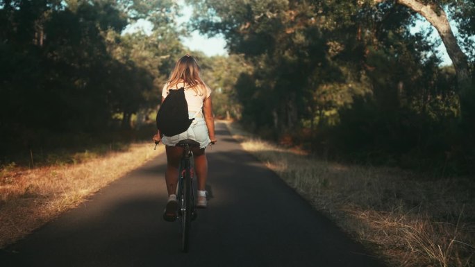 在森林路上骑自行车的妇女的后视图