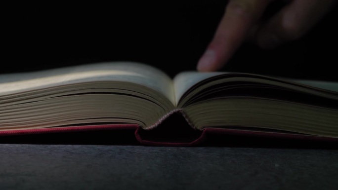 一只手在一本旧书上的特写，一位老人的手指沿着一本档案书的线条移动。有选择性的重点。休闲读书。一个老人