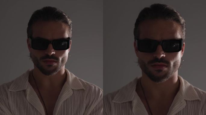 性感的时尚男人戴着太阳镜，双臂折叠，看向一侧和向前，在灰色背景上性感地触摸嘴唇