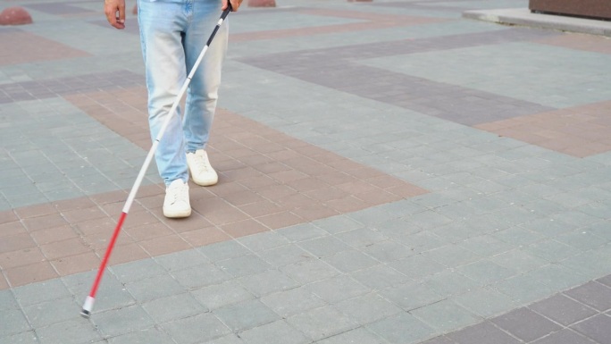 衣冠楚楚的盲人拄着一根长长的白手杖走在路边，近距离观察手杖和脚