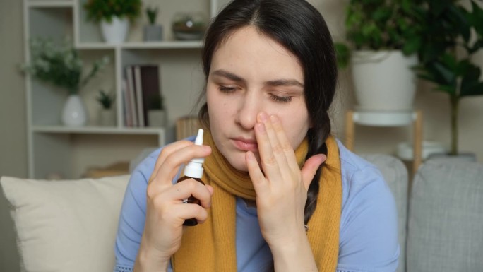 一位患有鼻炎的生病妇女将药喷进鼻子里。