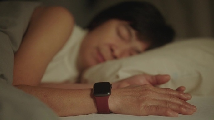 成熟的女人在晚上睡觉时戴着智能手表。