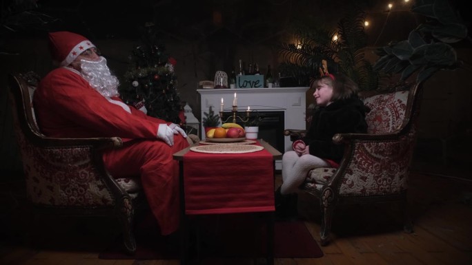 圣诞夜，可爱的小女孩和圣诞老人坐在餐桌旁