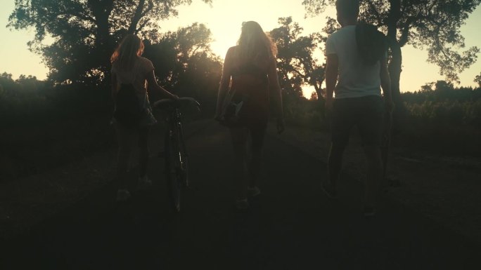 三个朋友骑着自行车和滑板走在森林路上的剪影