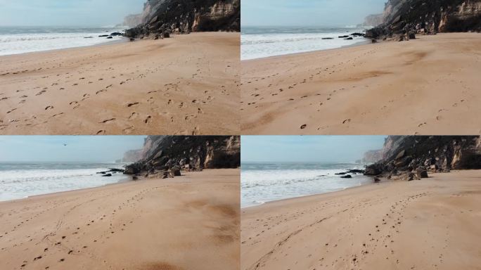 在葡萄牙莱里亚的纳扎雷岩石海岸，带着脚印在沙滩上飞行。低空拍摄