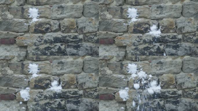 慢动作特写，雪球打在灰色的石墙上，溅起水花