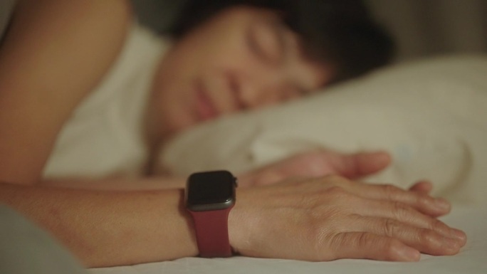成熟的女人在晚上睡觉时戴着智能手表。