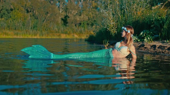 迷人美丽的鲁萨尔卡与大鱼尾躺在浅水河岸，肖像4K，普罗斯