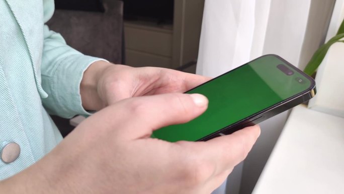 一名女子将录像带滚动到智能手机上，并将其展示给摄像头，这是一款带有绿色屏幕的智能手机特写镜头
