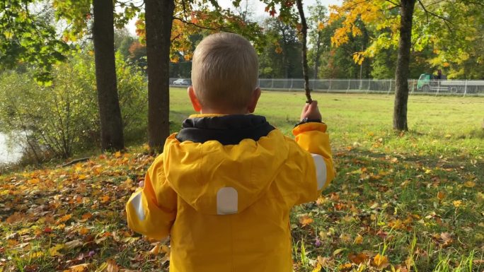 蹒跚学步的孩子穿着黄色的夹克，流着鼻涕走在秋天的公园里