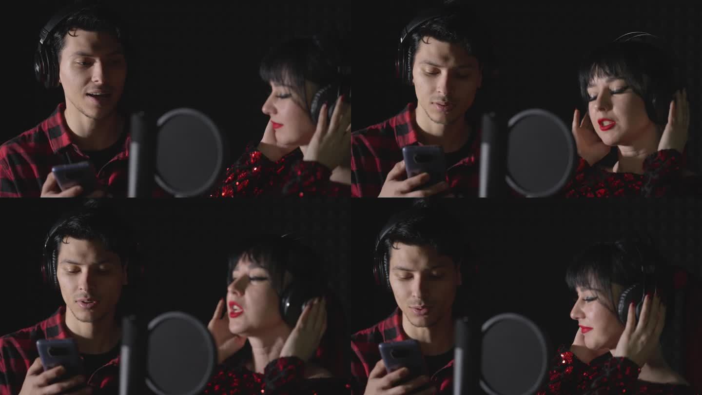一个男人和一个女人，有抱负的艺术家，站在录音棚里唱一首歌。这名男子看着智能手机屏幕上的歌词。
